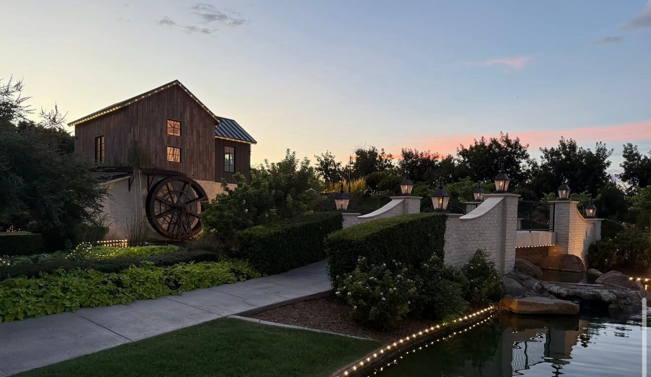 The mill at dusk with string lights along its roofline and lanterns on the bridge wall