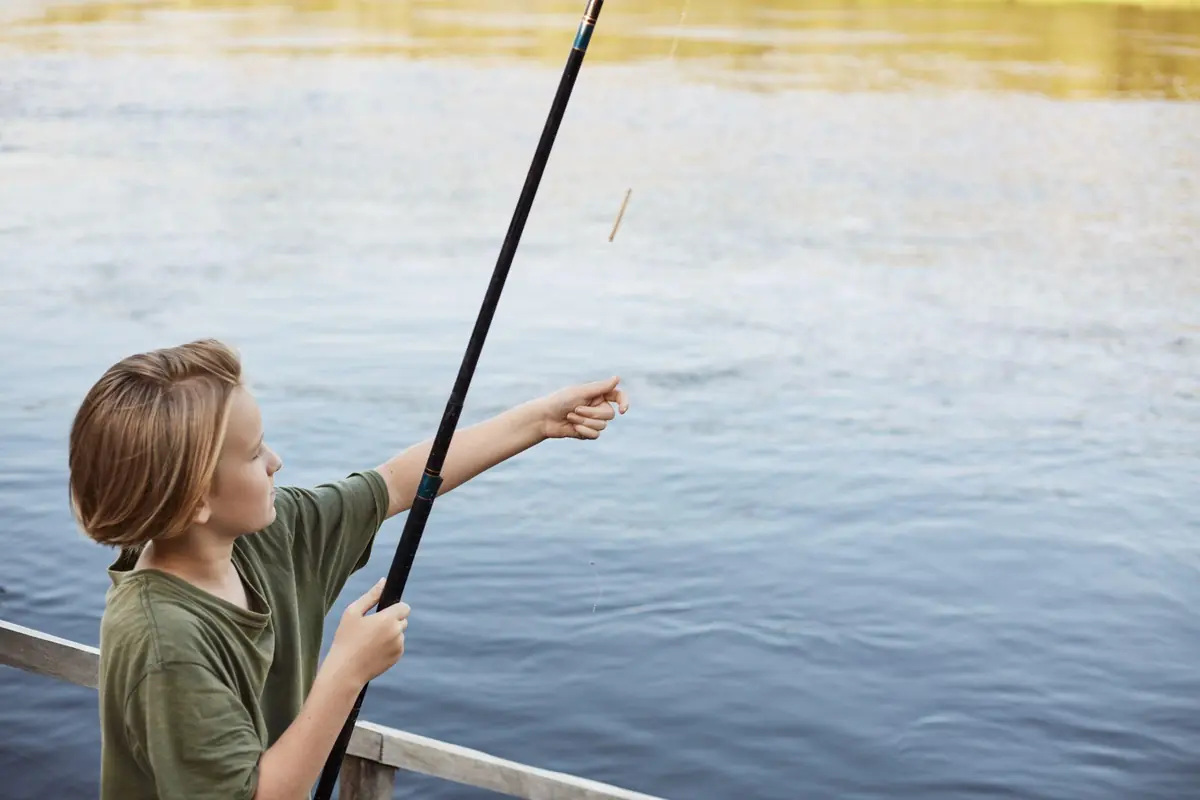 A child casting a long fishing pole out over the water of a lake